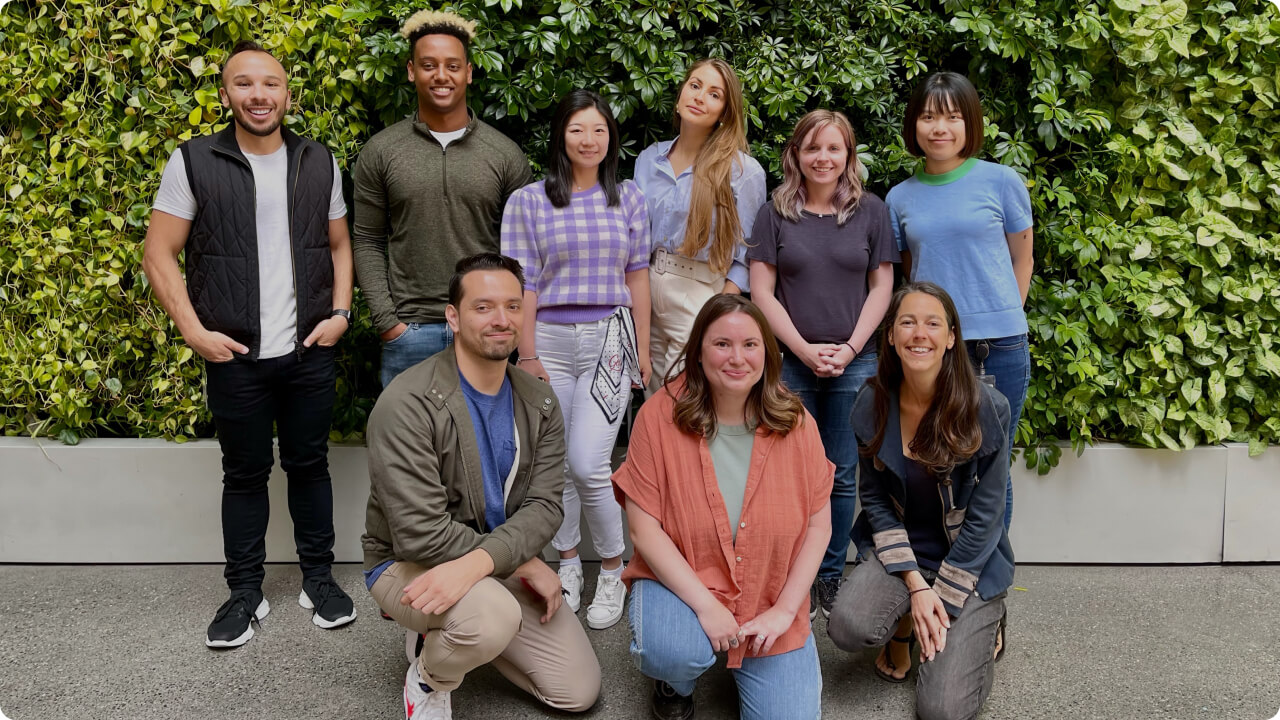 A group photo of our latest Connect Apprenticeship Program cohort. The apprentices are smiling, with three kneeling in front and five standing behind, next to the program lead. Behind the group is a living greenery wall.