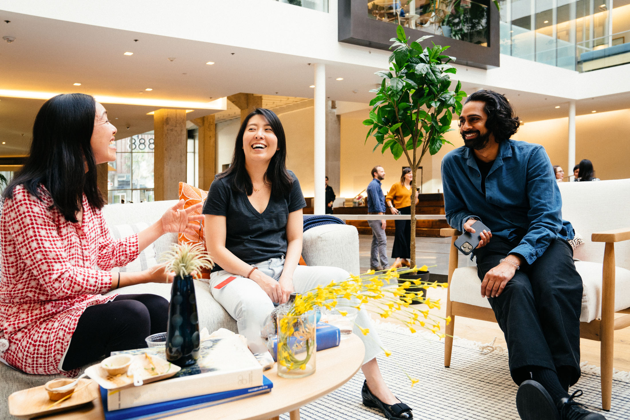 Three employees engaged in lively conversation while seated around a coffee table in the office atrium.