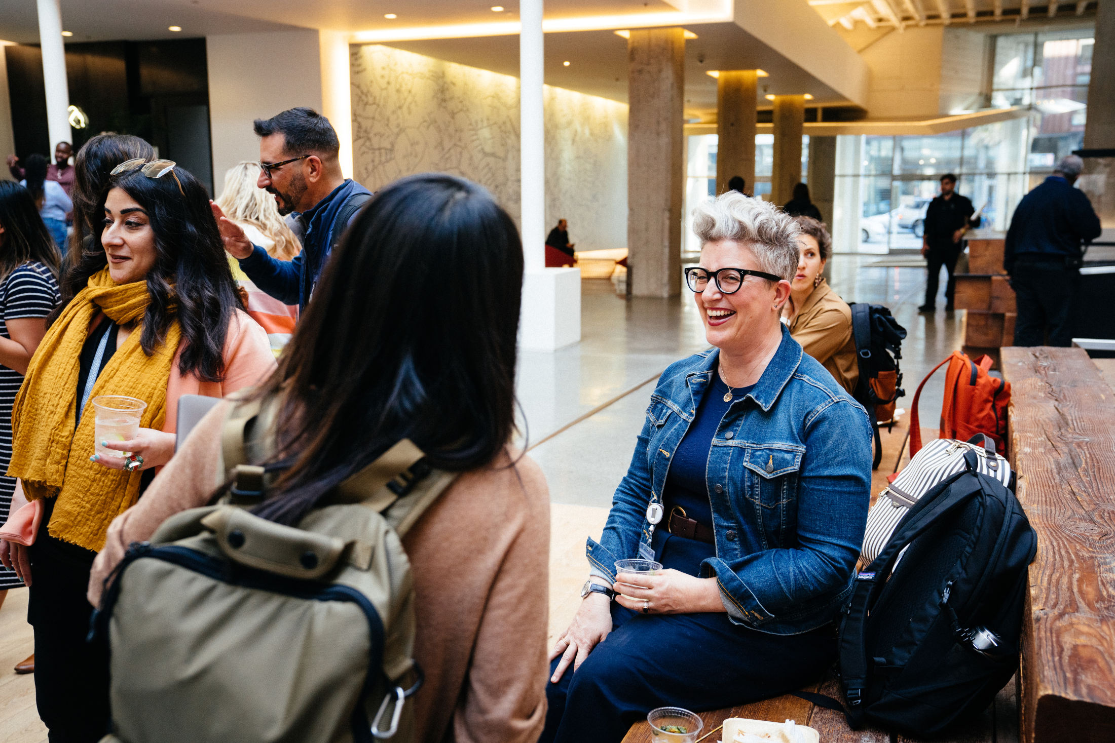 Airbnb team mates share joyful conversations and drinks with each other in the office atrium during a social event